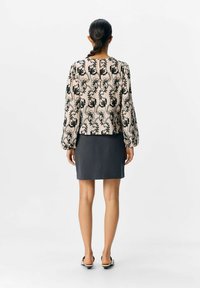 Motif floral noir brodé sur un haut beige à manches bouffantes, associé à une jupe noire ajustée et des chaussures plates.