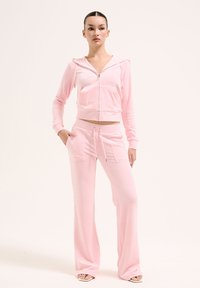 Haut zippé rose avec poches avant et pantalon assorti. Tissu doux, coupe décontractée, manches longues et taille à cordon.