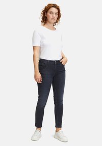 Ciemnoniebieskie wąskie dżinsy o średnim stanem, z kieszeniami z przodu i gładką fakturą, uzupełnione białą koszulką z krótkim rękawem.