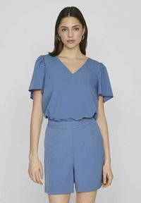 Haut bleu clair à manches courtes avec un col en V et un détail froncé aux épaules, assorti à un short ajusté. Tissu lisse, coupe décontractée.