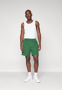 Pantalones cortos verdes de tela ligera, con una cinturilla elástica. Combinados con una camiseta sin mangas blanca y zapatillas blancas.