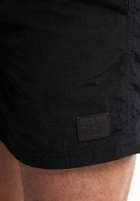Pantaloni scurți negri dintr-un material texturat, cu un etichetă cusută pe care scrie „Petrol Ind” în partea stângă jos.