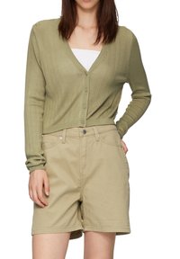 Olivgrüner, gerippter Cardigan mit V-Ausschnitt und Knopfverschluss, kombiniert mit beigen Shorts mit Fronttaschen und lockerer Passform.
