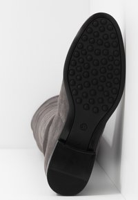 Botín de ante gris con suela de goma que presenta pequeños patrones circulares, mostrando la textura de la suela y un diseño de tacón liso. Talla 37 indicada.