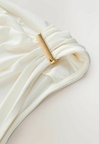 White fabric gathered with a gold metal accent. Features soft texture, smooth finish, and finished edge along the seam.