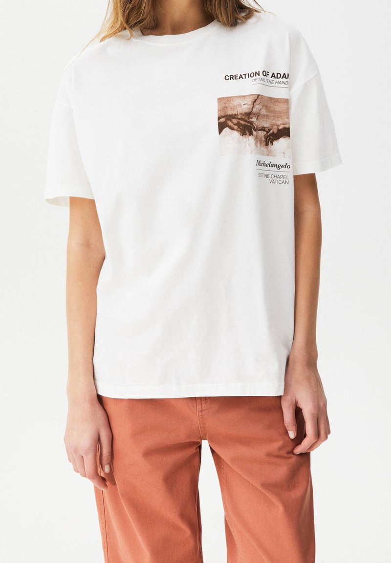 Camiseta de algodón blanca con un gráfico impreso en la parte frontal de "La creación de Adán" de Miguel Ángel, con texto que detalla la obra de arte. Corte relajado.