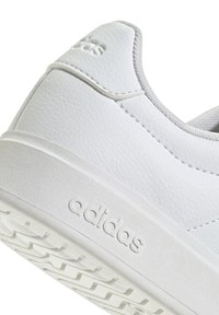 Tacón y suela de zapatilla Adidas blanca que muestran cuero texturizado y logo en relieve en la entresuela y la lengüeta del talón.
