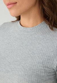 Grijze geribde top met een ronde halslijn en textuurstof. Het ontwerp bevat subtiele verticale strepen en een zachte afwerking.