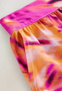 Top colorido con un cuello rosa, que presenta una tela vibrante de color naranja con patrones abstractos en púrpura y negro. Textura suave y diseño fruncido.