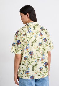 Kortærmet blomsterknaptrøje med en gul baggrund og flerfarvede blomster mønstre samt et afslappet fit design. Strukturstof.