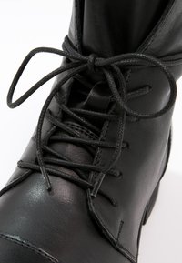 Black leather ankle boot with a rounded toe, featuring a textured surface, double-stitched detailing, and narrow matching laces.