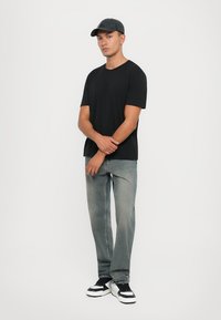 Svart kortermet t-skjorte kombinert med lysegrå jeans. Modellen har på seg en mørk caps og svart-hvite joggesko. Enkelt, minimalistisk design.