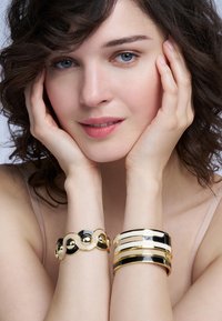 Bracelets en or et noir : l'un présente des courbes entrelacées avec des accents métalliques, l'autre a des bandes dorées brillantes et mates alternées.