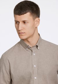 Camicia collare marrone chiaro con design a bottoni, texture morbida e bottoni bianchi. Vestibilità aderente con colletto strutturato.