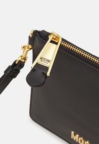 Svart läderpung med guldblixtlås, utrustad med en detaljerad dragkedja, präglat logotyp och en avtagbar rem. Slät textur.