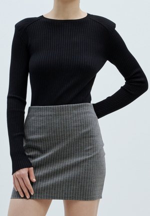 Schwarzes, geripptes Langarmoberteil mit rundem Ausschnitt, kombiniert mit einem grauen Rock mit weißen vertikalen Streifen und figurbetontem Design.