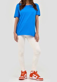 Bright blue short-sleeve t-shirt paired with white textured leggings and orange high-top sneakers featuring white accents.