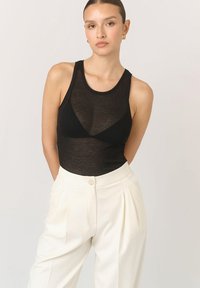 Czarna siateczkowa koszulka na ramiączkach o dopasowanym kroju i okrągłym dekolcie, zestawiona z wysokimi, plisowanymi białymi spodniami z przodu z zapięciem na guzik.