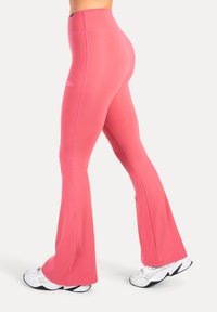 Roze flare legging gemaakt van rekbaar materiaal, met een hoge taille en contrasterende naden. Draagt witte sneakers.