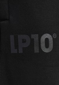 Zwarte stof met een gladde textuur waarop "LP10" in grote, glanzende grijze letters staat gedrukt. Het materiaal lijkt rekbaar en geschikt voor actieve kleding.