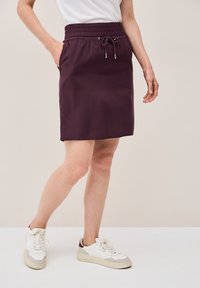 Gonna viola a vita elastica con cordino regolabile, dotata di tasche laterali, abbinata a sneakers bianche. Tessuto con superficie liscia e taglio alla lunghezza del ginocchio.