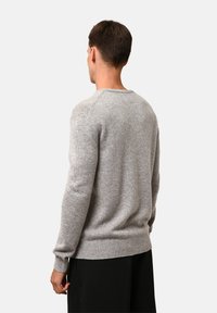 Grå ulltröja med rundad halsringning, ribbstickade manschetter och fåll. Mjuk textur, avslappnad passform och enkel design utan utsmyckningar.