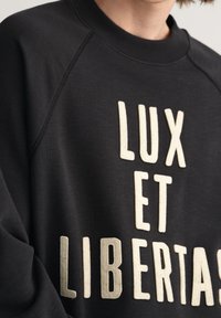 Felpa nera con scollo rotondo e maniche raglan, con testo beige che recita "LUX ET LIBERTAS" in un carattere in grassetto.