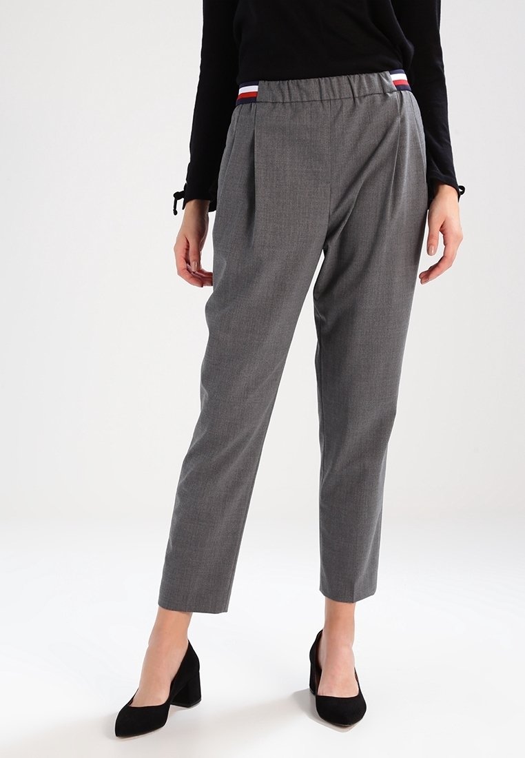 Femme portant un pantalon gris fuselé avec une taille élastique rayée et un haut noir à manches longues, assorti à des chaussures noires à talons blocs.