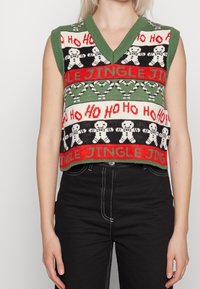 Grünes, gestricktes ärmelloses Weste mit einem V-Ausschnitt, festlichen Mustern von Lebkuchenfiguren, "Jingle" und "Ho Ho Ho" in Rot und Schwarz.