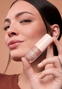 Pupa Wonder Me Shake Contour en un frasco cilíndrico transparente con una tapa rosa pálido, presentado sobre un fondo liso de color melocotón apagado.