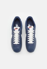 Navy blue leather sneakers with white laces, featuring a white swoosh logo and padded collar for comfort. Textured insole.