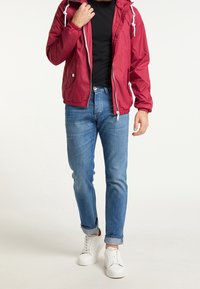 Chaqueta ligera roja con cremallera y cordones blancos, camiseta negra, vaqueros ajustados azules y zapatillas blancas. Tela suave, ajuste informal.