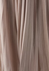 Gros plan sur un tissu beige avec des plis verticaux et une texture subtile à côtes horizontales créant des ombres douces.