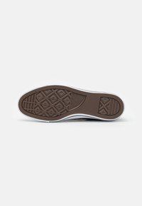 Semelle d'une basket montrant une bande de roulement en caoutchouc marron avec des motifs géométriques et le logo Converse All Star au centre.