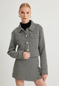 Jasje met zwart-wit houndstoothpatroon, met parelknopen, een kraag en een cropped ontwerp, gecombineerd met een bijpassende rok.
