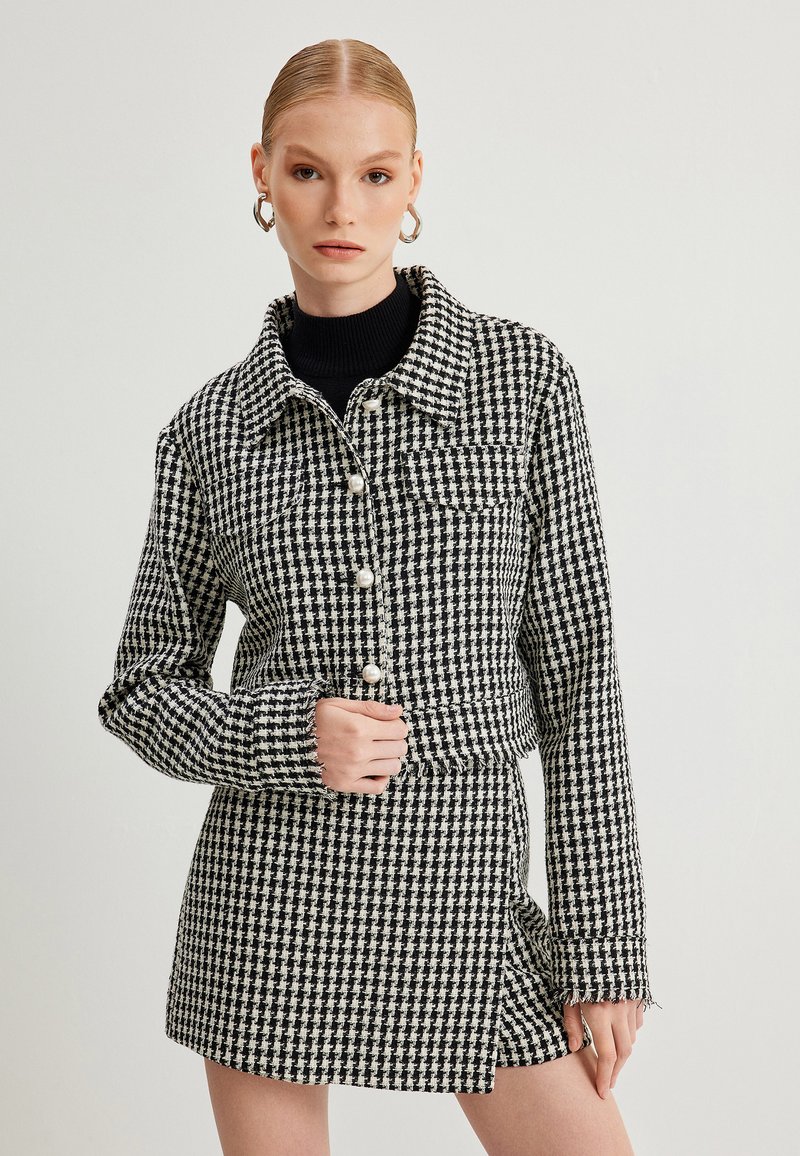Jasje met zwart-wit houndstoothpatroon, met parelknopen, een kraag en een cropped ontwerp, gecombineerd met een bijpassende rok.