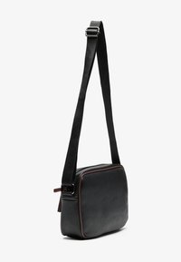Sac à épaule rectangulaire noir en matériau texturé, au design plat, avec une sangle foncée et un passepoil marron le long des bords.