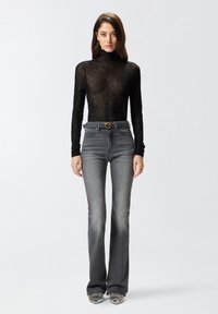 Top negro transparente de manga larga con detalles de brillo sutil, combinado con jeans ajustados de campana grises y zapatos con acentos metálicos.
