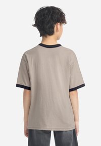 Beige bomull t-skjorte med korte ermer, kontrastfarge i mørk marineblå langs nakken og erme kantene, samt en rund nederkant. Ingen synlige mønstre eller design.