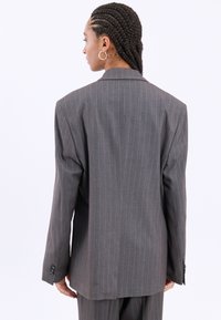 Blazer grigio a righe con un fit rilassato, revers a punta e polsini con due bottoni, che mostra una texture liscia e linee pulite dalla parte posteriore.