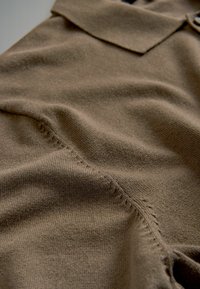 Brązowa dzianinowa koszulka polo z kołnierzykiem, charakteryzująca się gładką fakturą i widocznymi detalami szycia wzdłuż szwów.