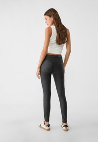 Črne skinny jeans z visokim pasom, elastičen material in dva zadnja žepa, v kombinaciji z belo brezrokavno majico in svetlimi športnimi copati.