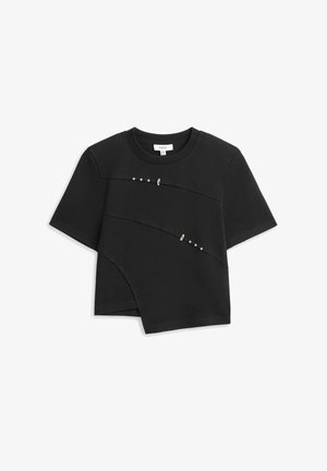 T-shirt noir à manches courtes avec ourlet asymétrique et deux rangées diagonales de petits clous argentés et épingles de sûreté sur le devant.
