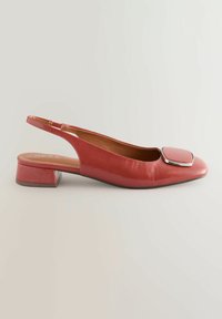 Punainen synteettinen slingback-kengä, jossa on neliömäinen kärki, matala lohkokorko ja glossy-pinta. Kengässä on metallinen neliökoriste kärjessä.