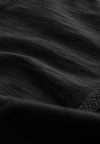 Černá texturovaná látka s jemným leskem, která má měkký, hladký povrch a jemné splývání. Detail v rohu zahrnuje síťovinu.