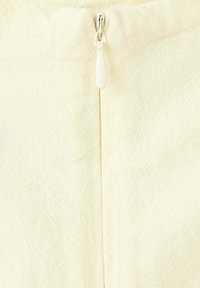 Gros plan d’un tissu de couleur crème avec une fermeture éclair blanche centrée et un motif texturé visible sur le matériau.