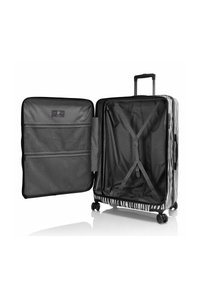 Maleta rígida con patrón de cebra, con un mango retráctil, cuatro ruedas, compartimentos con cremallera y un interior negro con correas cruzadas.