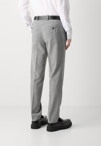 Pantaloni grigi su misura con un sottile motivo a quadri, frontale piatto, due tasche posteriori e cintura nera, abbinati a scarpe nere.