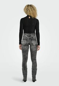 Maglietta nera a coste con maniche lunghe e dettaglio a chiave sul retro, abbinata a jeans grigi a vita alta effetto lavaggio acido e stivali cowboy grigi.