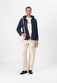 Ναυτικό φλις μπουφάν με κουκούλα, κρεμ πουκάμισο με κόκκινα και μπλε γράμματα, μπεζ παντελόνι και μαύρες loafers. Ελαφρύ υλικό, μπροστινό φερμουάρ.